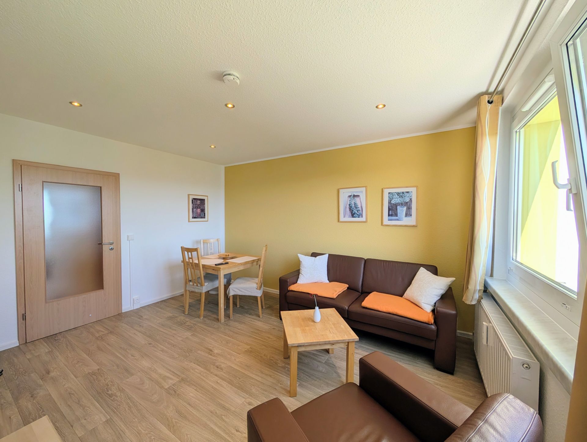 Wohnzimmer mit Blick Richtung Essecke und Sofa inklusive Couchtisch, Sessel und 3 Bildern an den Wänden