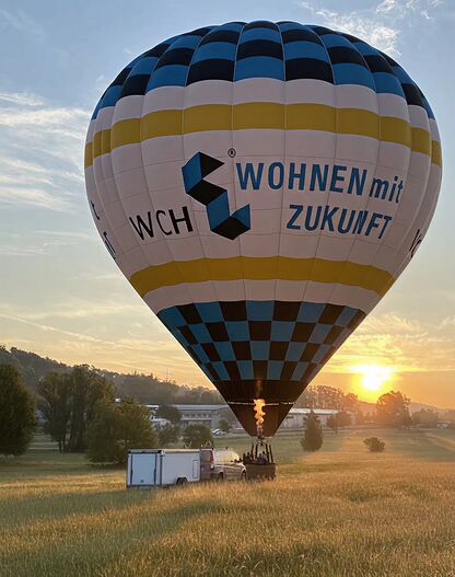Heißluftballon mit Werbung "WCH Wohnen mit Zukunft" beim Start im Sonnenuntergang.