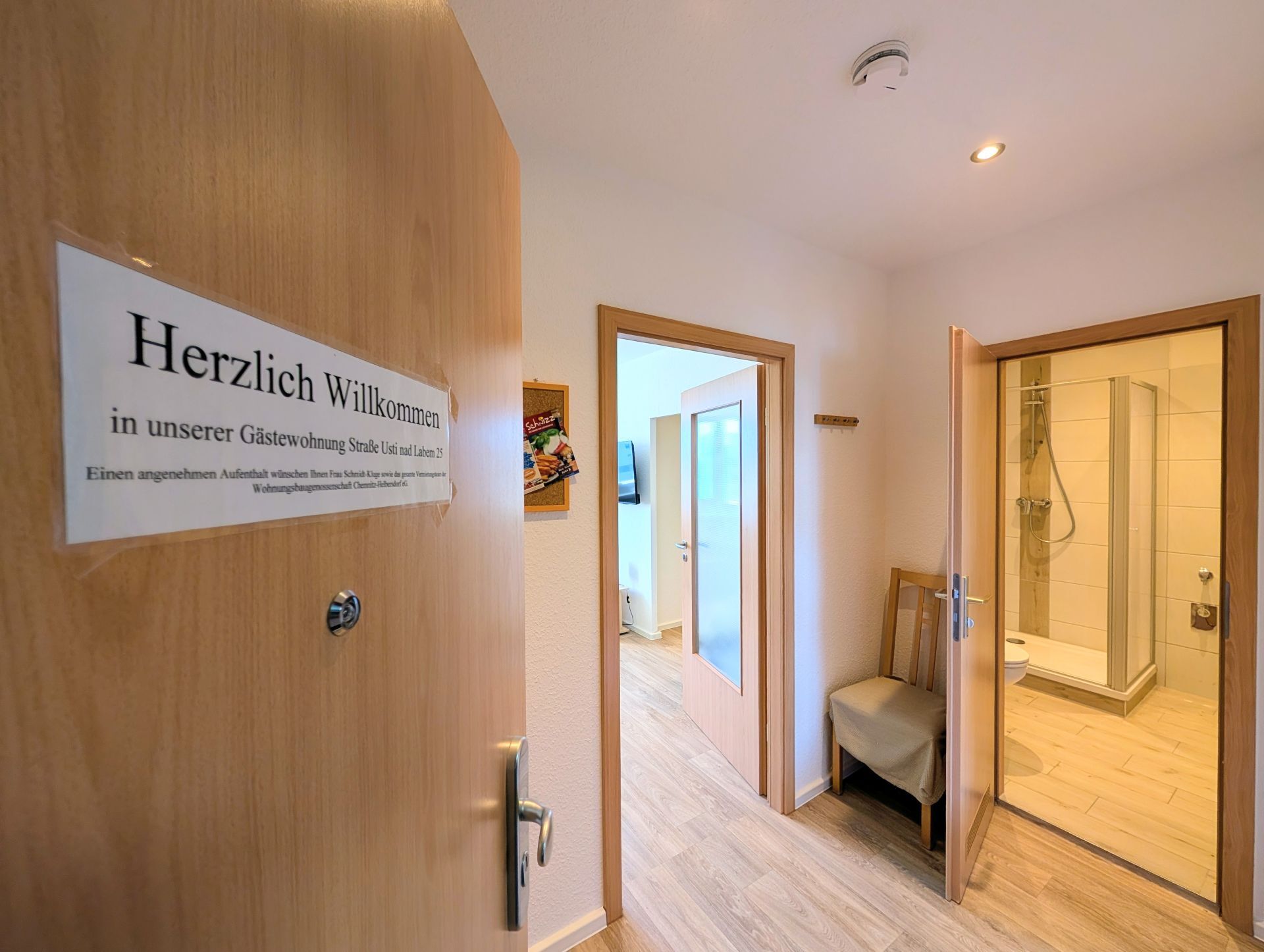 geöffnete Wohnungstür mit Herzlich-Willkommen-Schild, die sowohl einen Blick in den Flur als auch ins Badezimmer und ins Wohnzimmer erlaubt