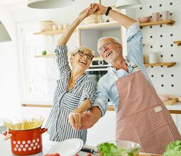 Glückliches Paar in gestreiften Schürzen beim gemeinsamen Kochen in moderner Küche.